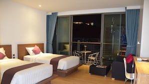 Een hotelkamer met twee bedden, een balkon met een tafel en stoelen, en een bureau met een stoel.