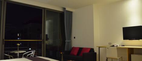 A hotel room with two beds, a desk, a chair, a TV, and a balcony with a table and chairs.