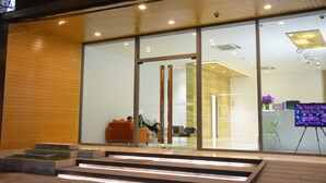 Een modern gebouw met grote glasramen, een houten gevel en een receptie met een prikbord waarop informatie staat.