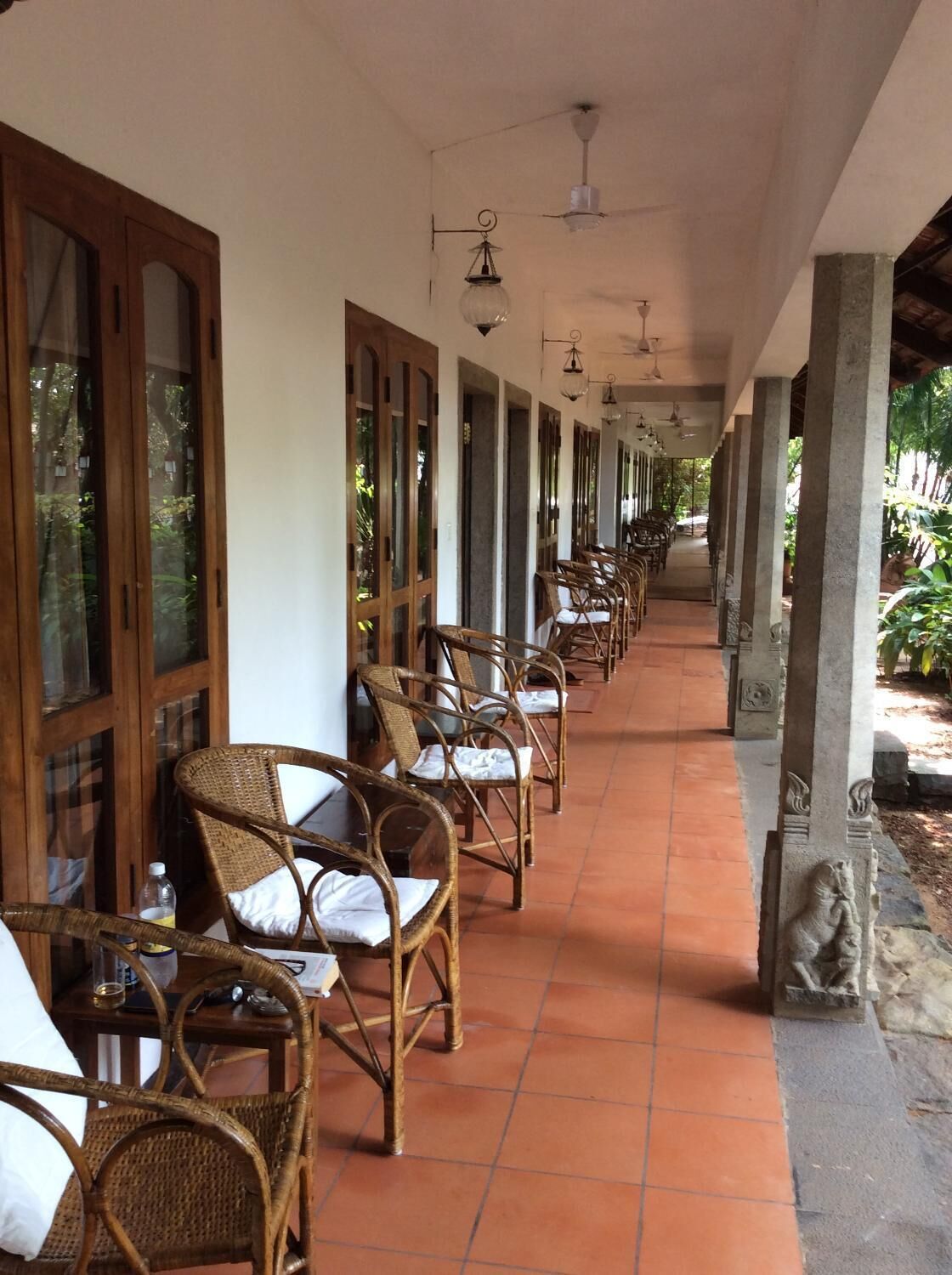 A covered outdoor seating area with wicker chairs and tables, large windows, and a tiled floor.