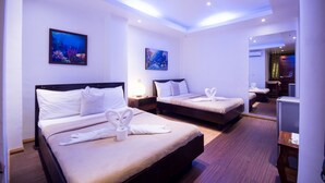 A hotel room with two beds, each with white linens and towels. There are wall-mounted paintings of underwater scenes. The room has a wooden floor and a ceiling with recessed lighting. - Deparis Beach Resort (Boracay Island)