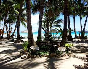 A sign for Decaris Resort surrounded by palm trees and beach chairs.