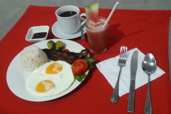 A breakfast plate with eggs, meat, and vegetables, a cup of coffee, and a glass of juice on a red tablecloth.