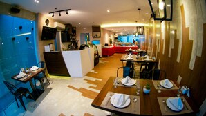A modern restaurant with wooden tables and chairs, a bar area, and a kitchen in the background. - Zerenity Hotel & Suites (Cebu City)