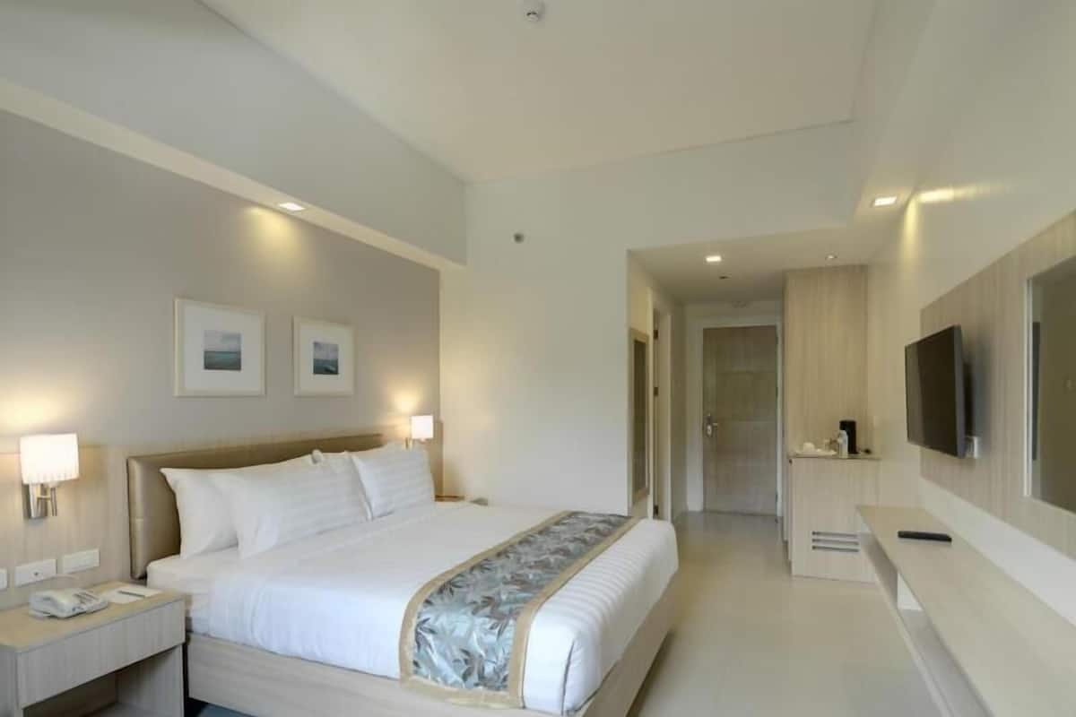 A modern hotel room with a large bed, bedside lamps, a flat-screen TV, and a hallway leading to a bathroom.