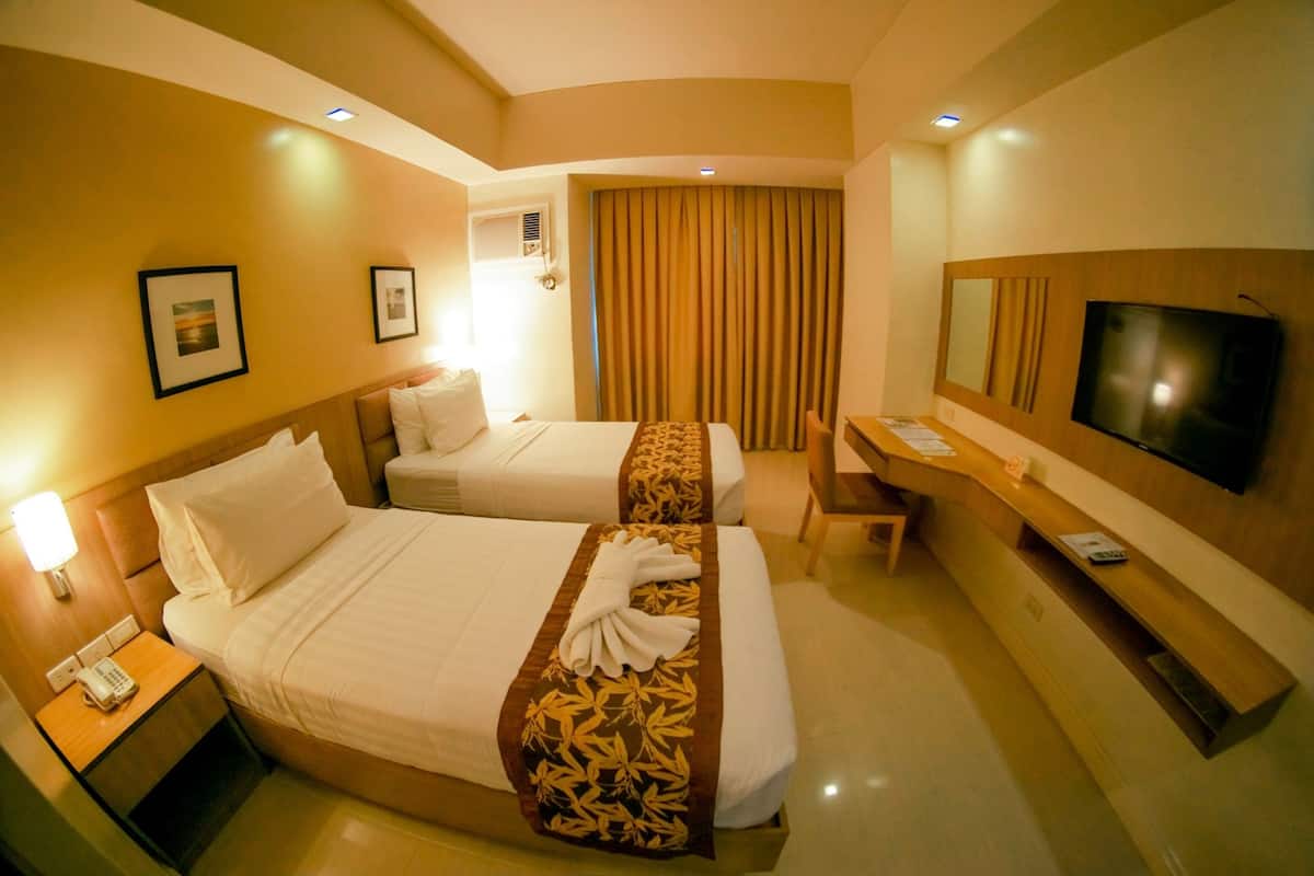 A hotel room with two beds, a desk, a TV, and a bathroom.
