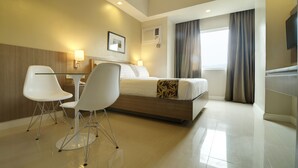 A hotel room with a bed, two white chairs, a desk, a flat-screen TV, and a window with curtains. - Zerenity Hotel & Suites (Cebu City)