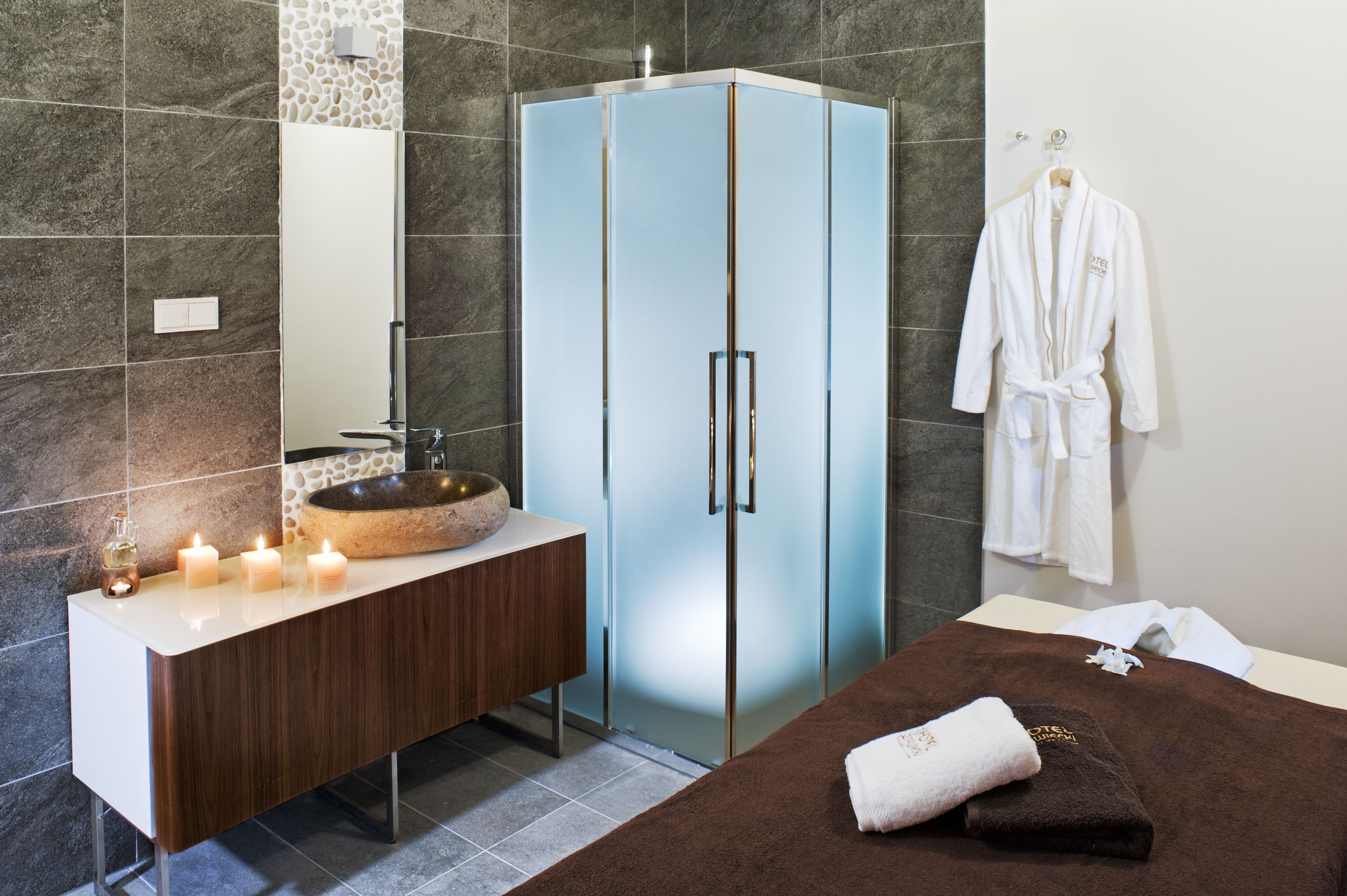 Un baño moderno con un tocador de madera, un armario de vidrio, un lavabo con cuenca de piedra y una toalla en la cama.