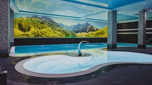 Une piscine intérieure moderne offrant une vue panoramique sur les montagnes, ainsi qu’un jacuzzi et un espace de détente.