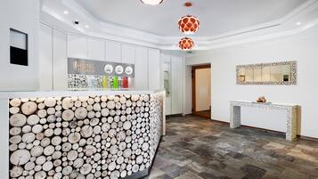 A hotel reception area with a modern design, featuring a central counter with a unique wood log display, a reception desk, and a decorative mirror on the wall.