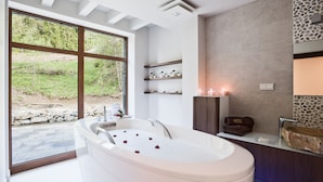 Une salle de bain moderne avec une baignoire sur pieds, une grande fenêtre donnant sur un espace verdoyant et un mur en pierre intégrant un lavabo.
