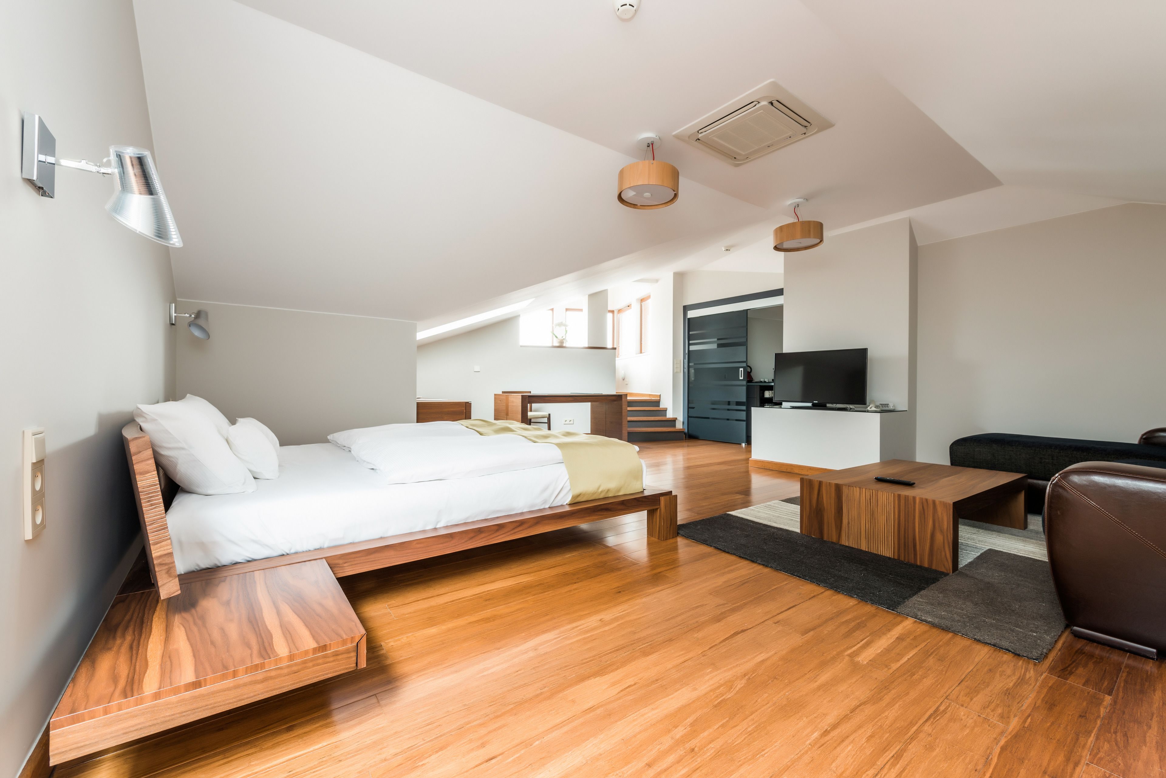 A modern bedroom with a wooden bed, a desk, a chair, and a TV.