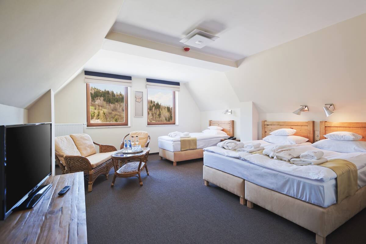 Ein Hotelzimmer mit Fernseher, zwei Betten, einer Schlafcouch und einem Esstisch.