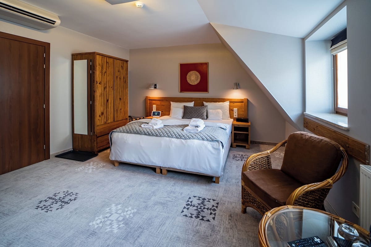 Ein Hotelzimmer mit einem großen Bett, einem Holzschrank und einer Sitzecke mit Sessel und Tisch.