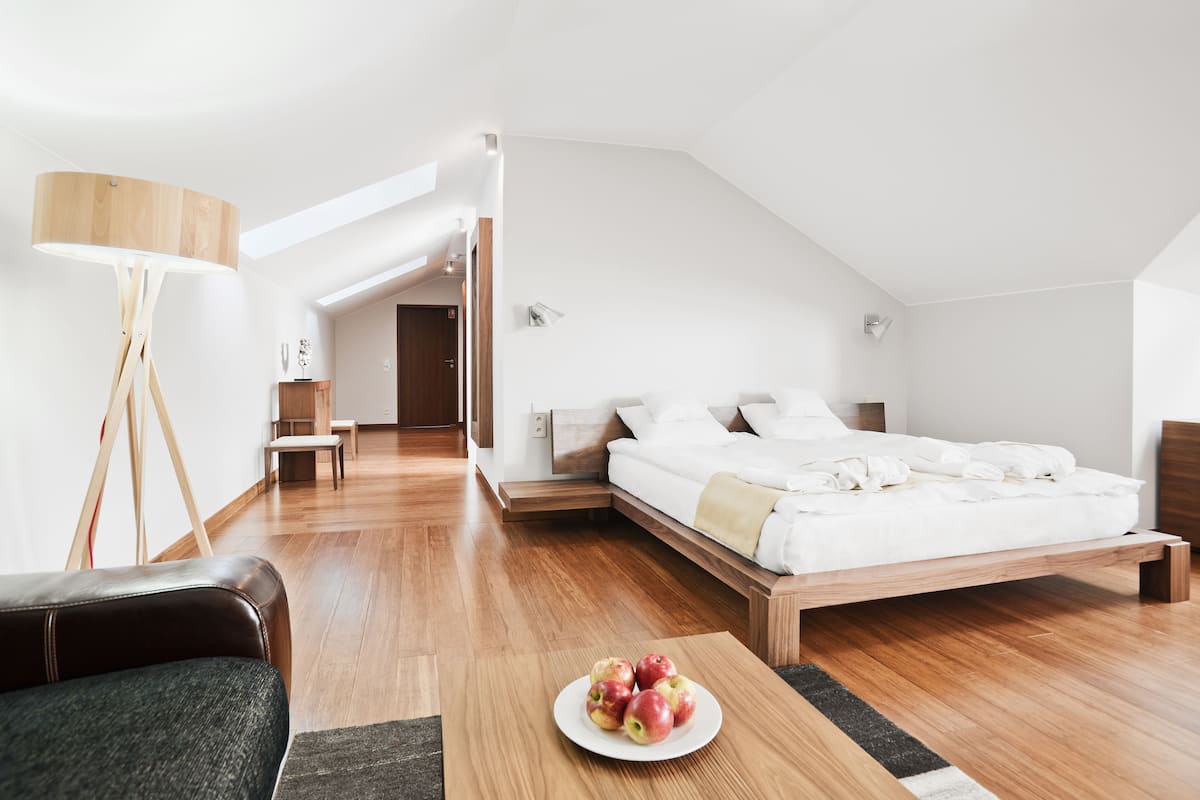 Ein modernes Schlafzimmer mit einem hölzernen Bett, einem Nachttisch, einer Stehlampe und einer Schale Äpfel auf dem Boden.