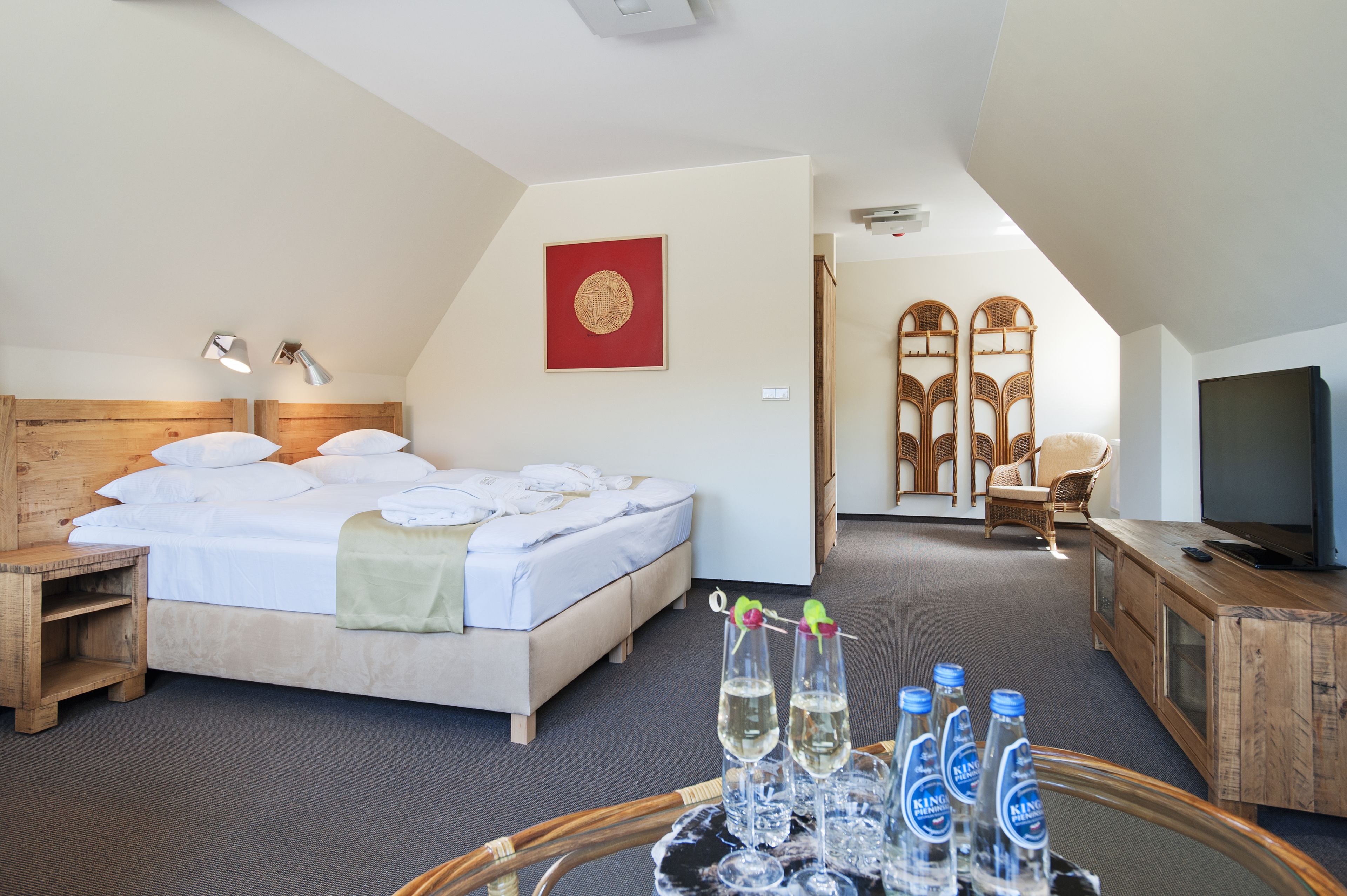 Et hotelværelse med en seng, natborde, et fjernsyn og et bakke med flasker og glas.