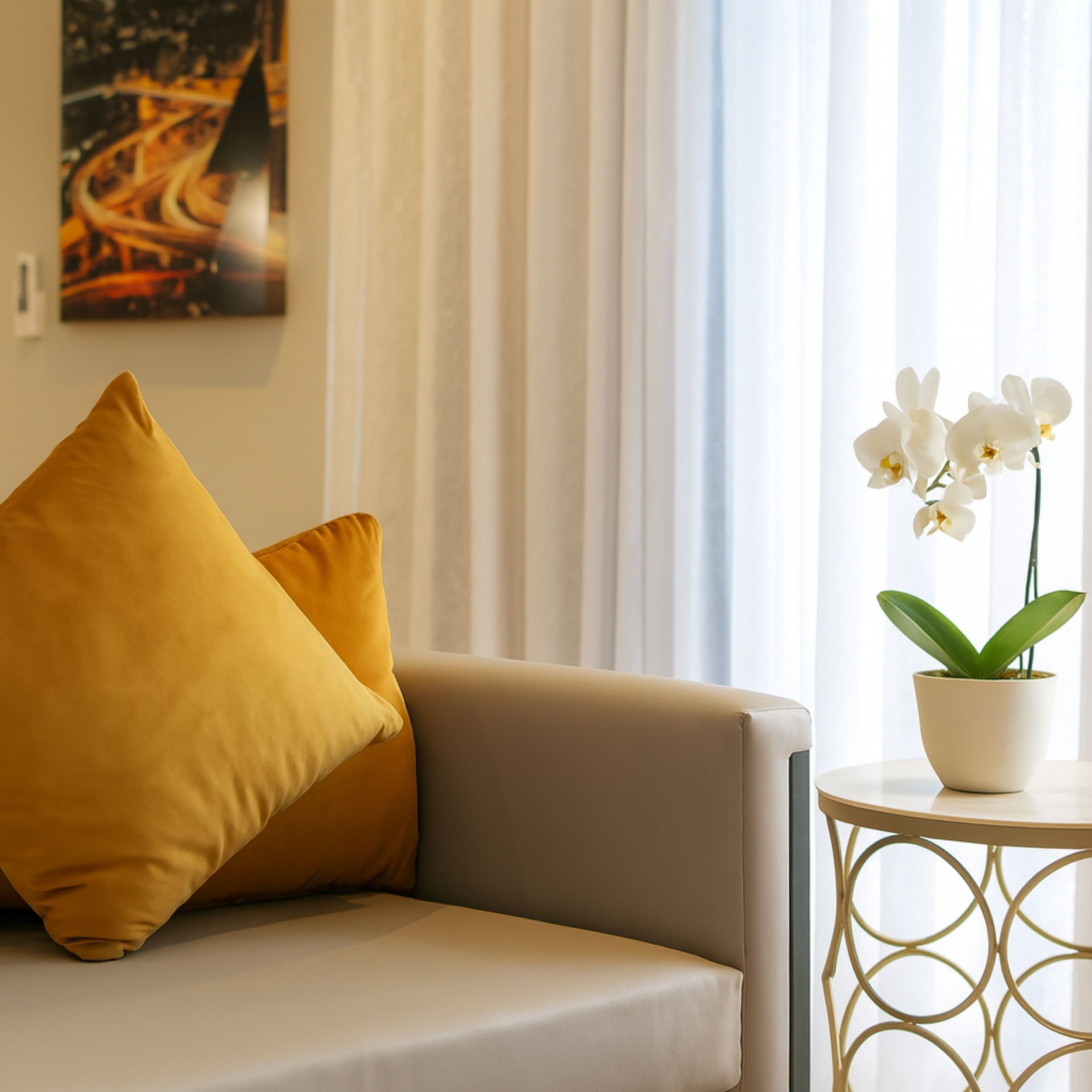A modern living room with a sofa, a small round table, and a potted orchid.