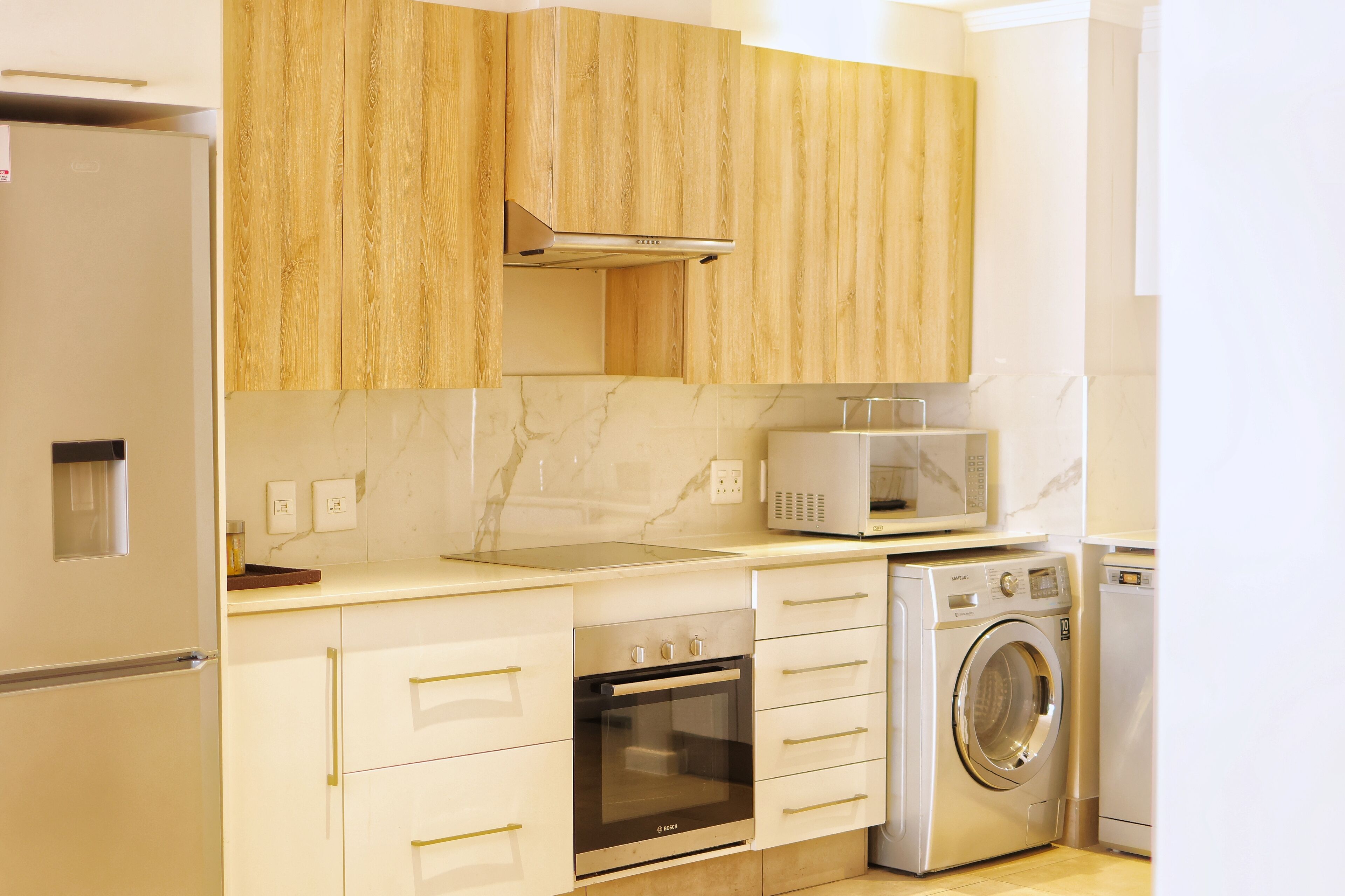 A modern kitchen with wooden cabinets, a built-in oven, a microwave, and a washing machine.
