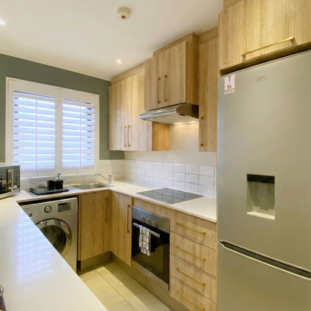 A modern kitchen with wooden cabinets, a stainless steel refrigerator, a built-in oven, and a dishwasher.