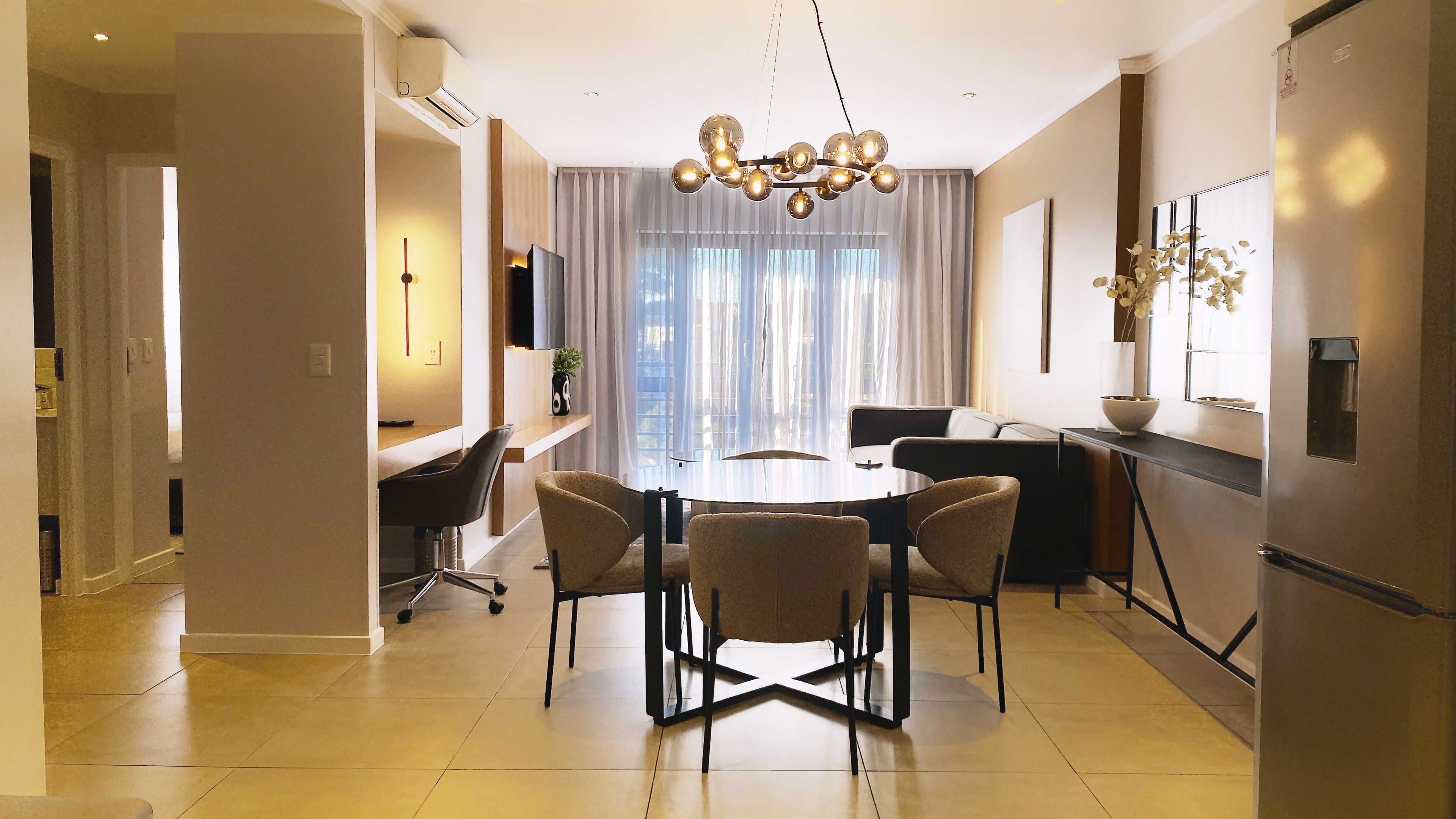 A modern dining area with a round table, four chairs, and a unique chandelier.