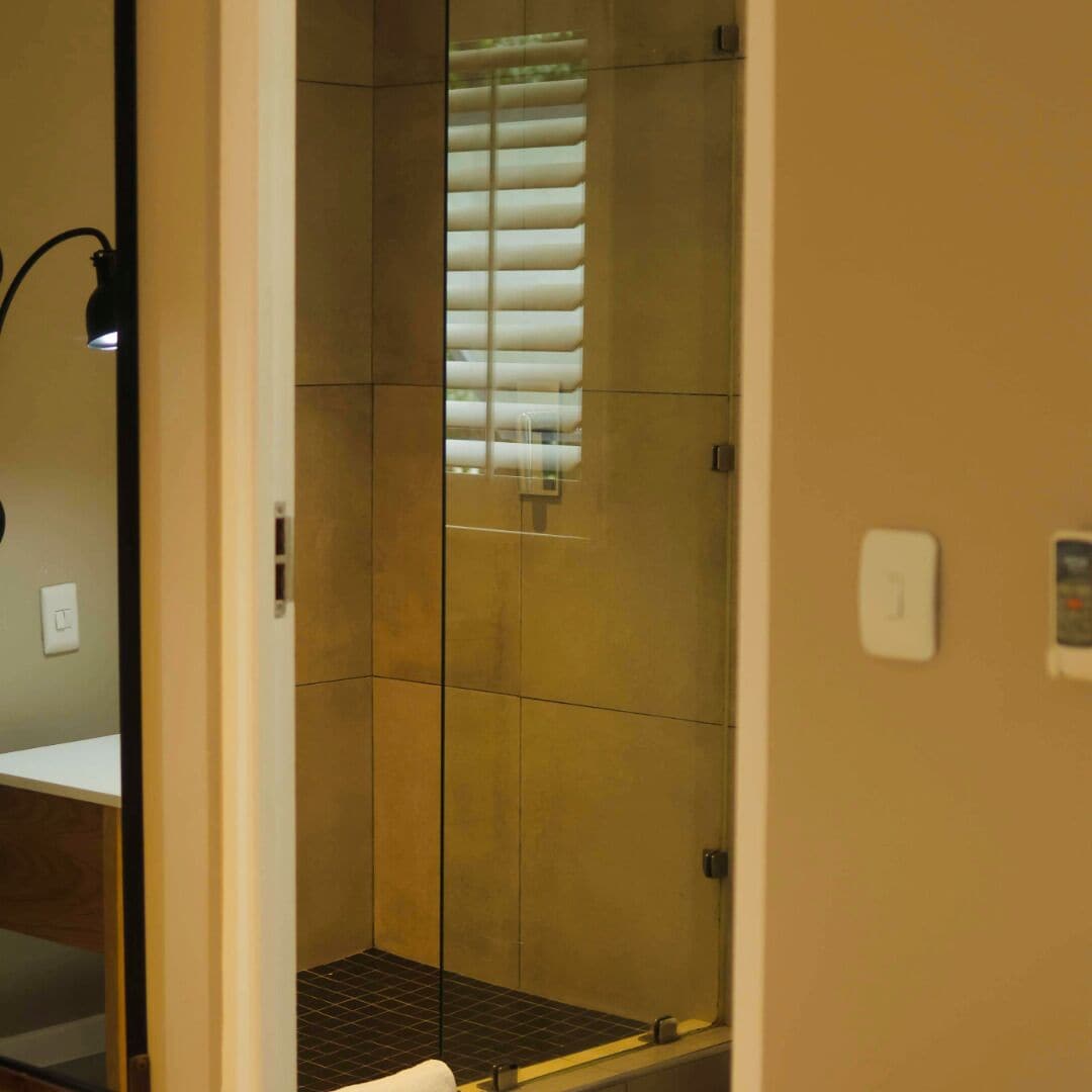 Une douche avec une porte en verre, un porte-serviettes et un luminaire.