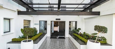 A modern building entrance with a reception desk, potted plants, and a tiled pathway.