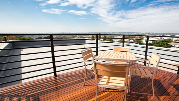 Eine Holzterrasse mit Tisch und Stühlen mit Blick auf eine Stadtlandschaft.