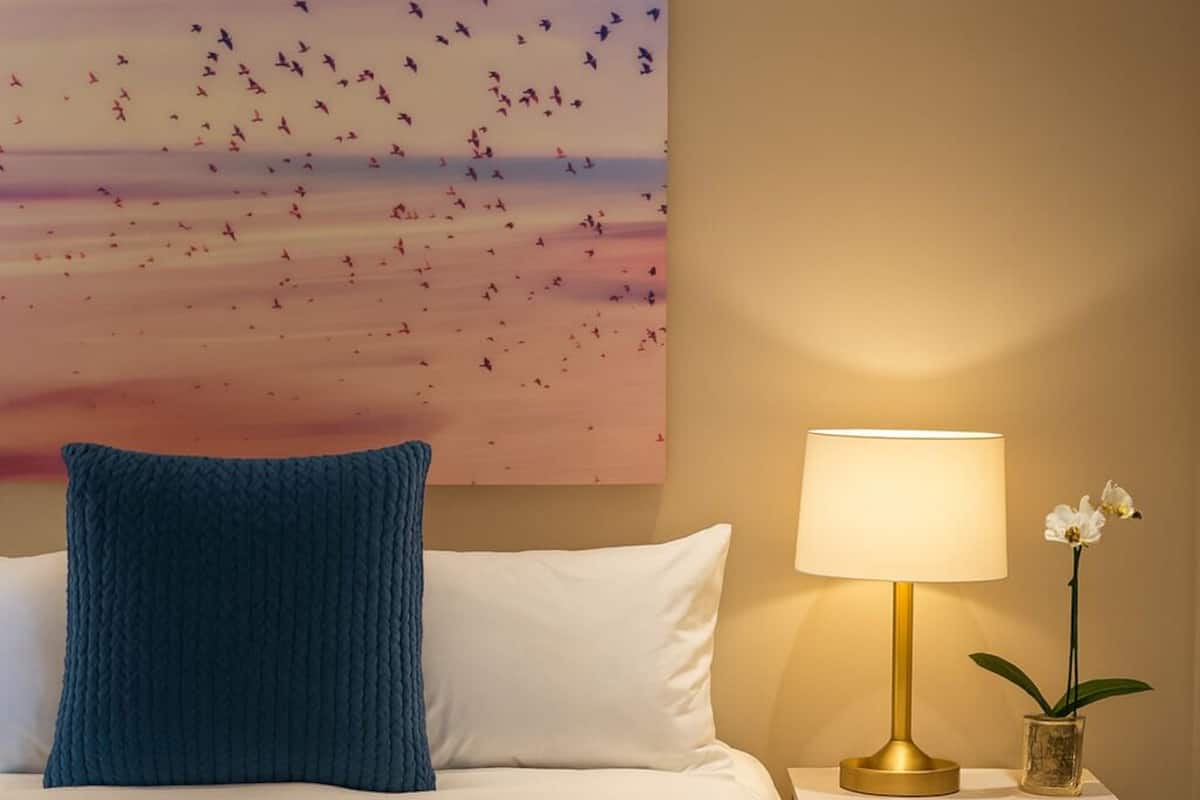 A neatly made bed with a blue pillow, a bedside lamp, and a small plant on a wooden nightstand.