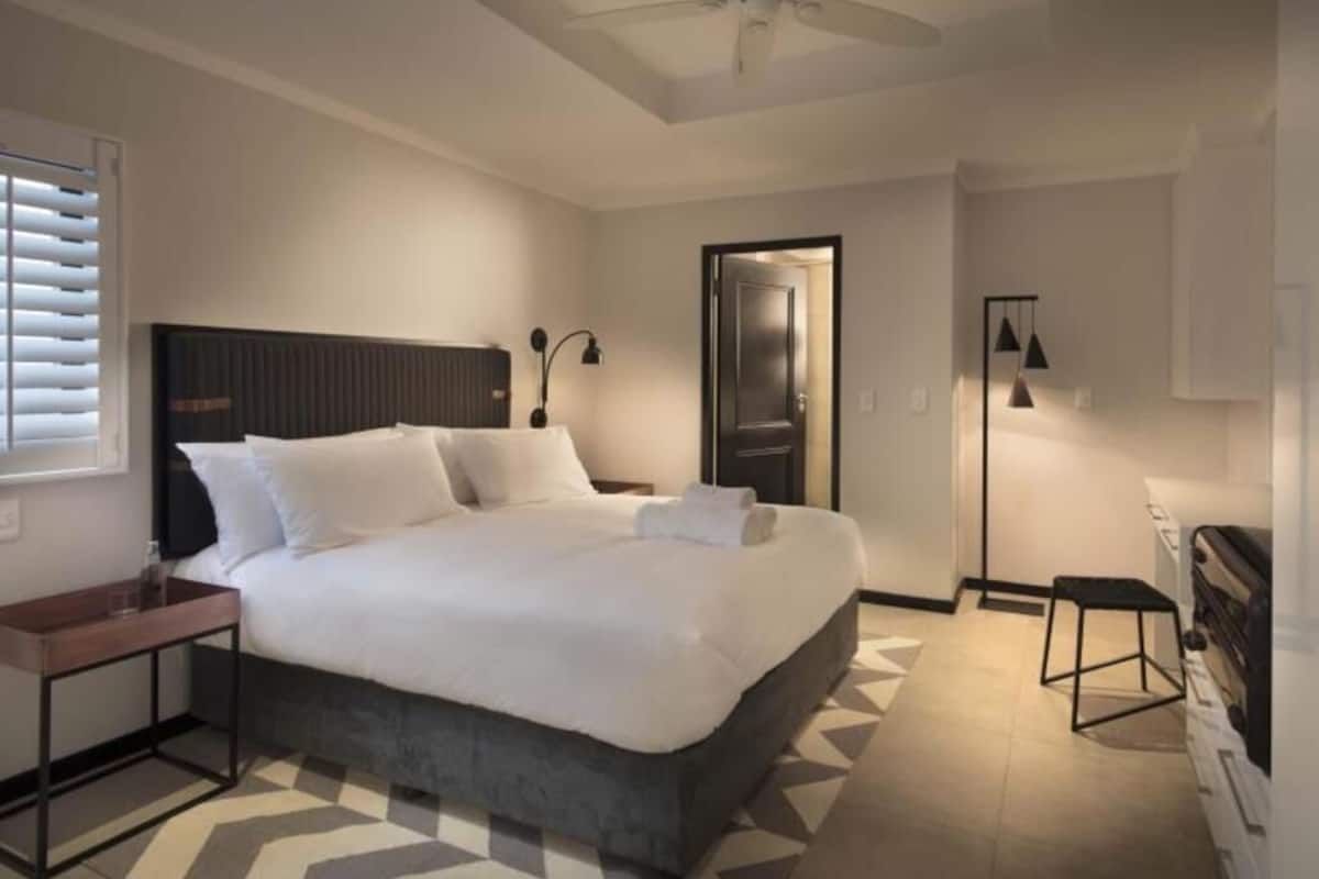 A modern hotel room with a large bed, a ceiling fan, a bedside table, a nightstand, a desk, and a chair.