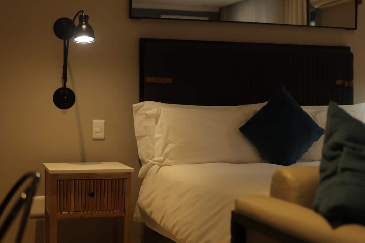 A neatly made bed with white and dark blue pillows, a bedside lamp, and a wooden nightstand.