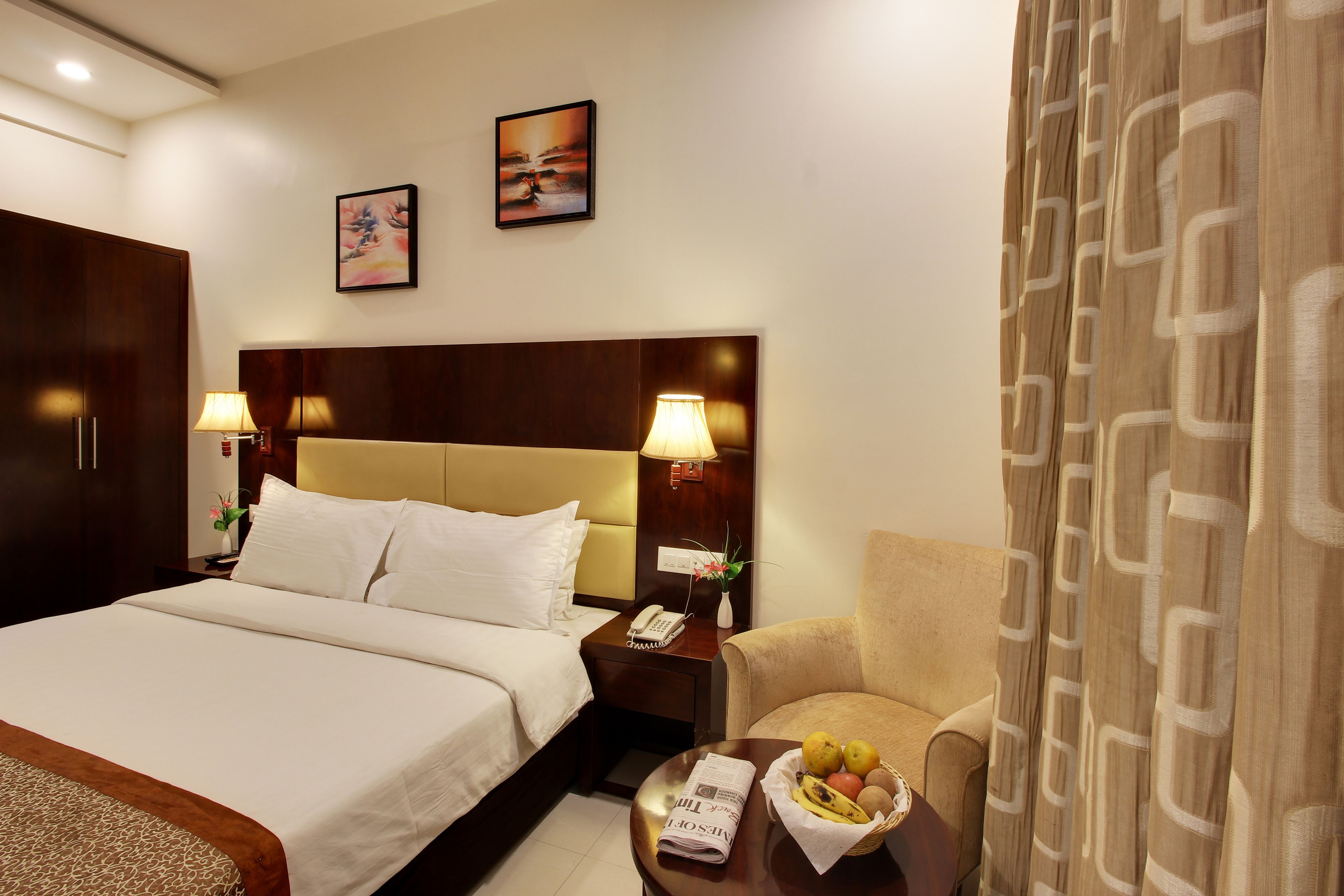 A hotel room with a large bed, a nightstand with a lamp, a chair, and a table with fruit.