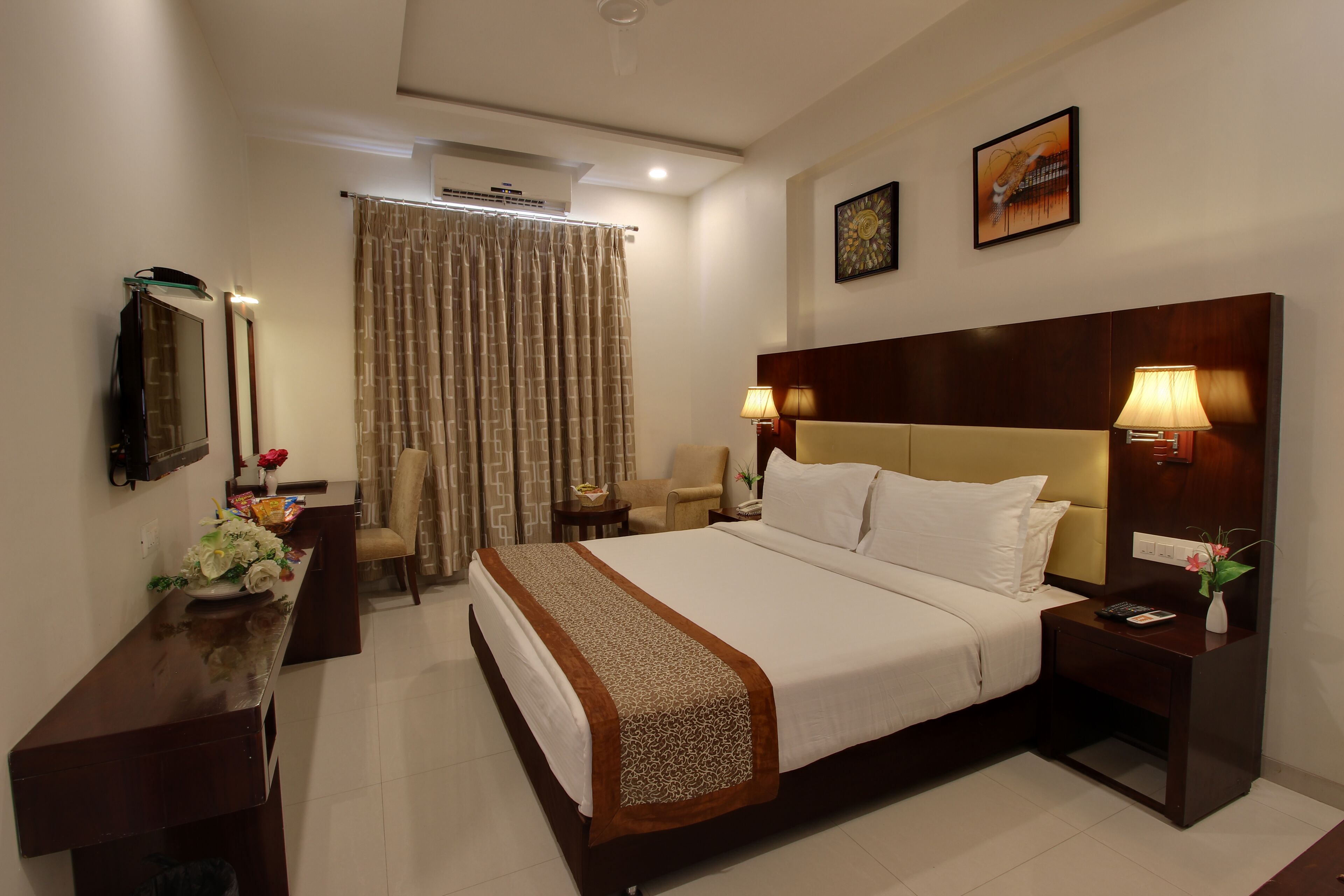 A hotel room with a bed, bedside tables, a desk, a chair, a TV, and a window with curtains.