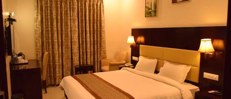 A hotel room with a bed, two bedside lamps, a chair, a desk, and an air conditioning unit.