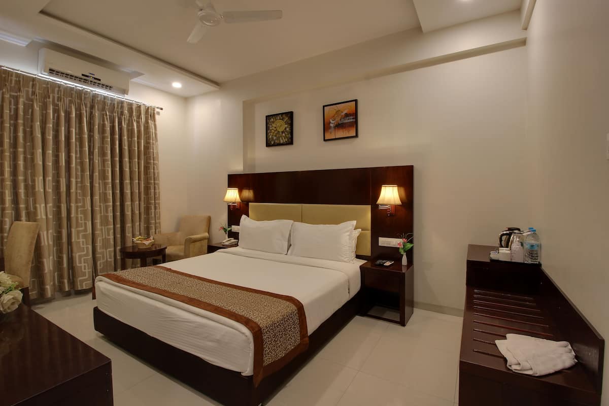 Une chambre d’hôtel comprenant un grand lit, deux tables de chevet, une petite table, un bureau, une chaise, un banc, un ventilateur de plafond et deux lampes fixées au mur.