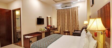 A hotel room with a bed, bedside table, lamp, and a desk with a chair.