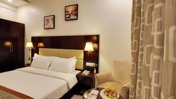Habitación de hotel con una cama grande, lámparas de noche, mesita de noche con teléfono, una silla y una mesa con fruta.