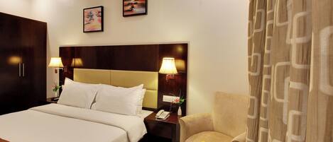 A hotel room with a large bed, bedside lamps, a nightstand with a phone, a chair, and a table with fruit.