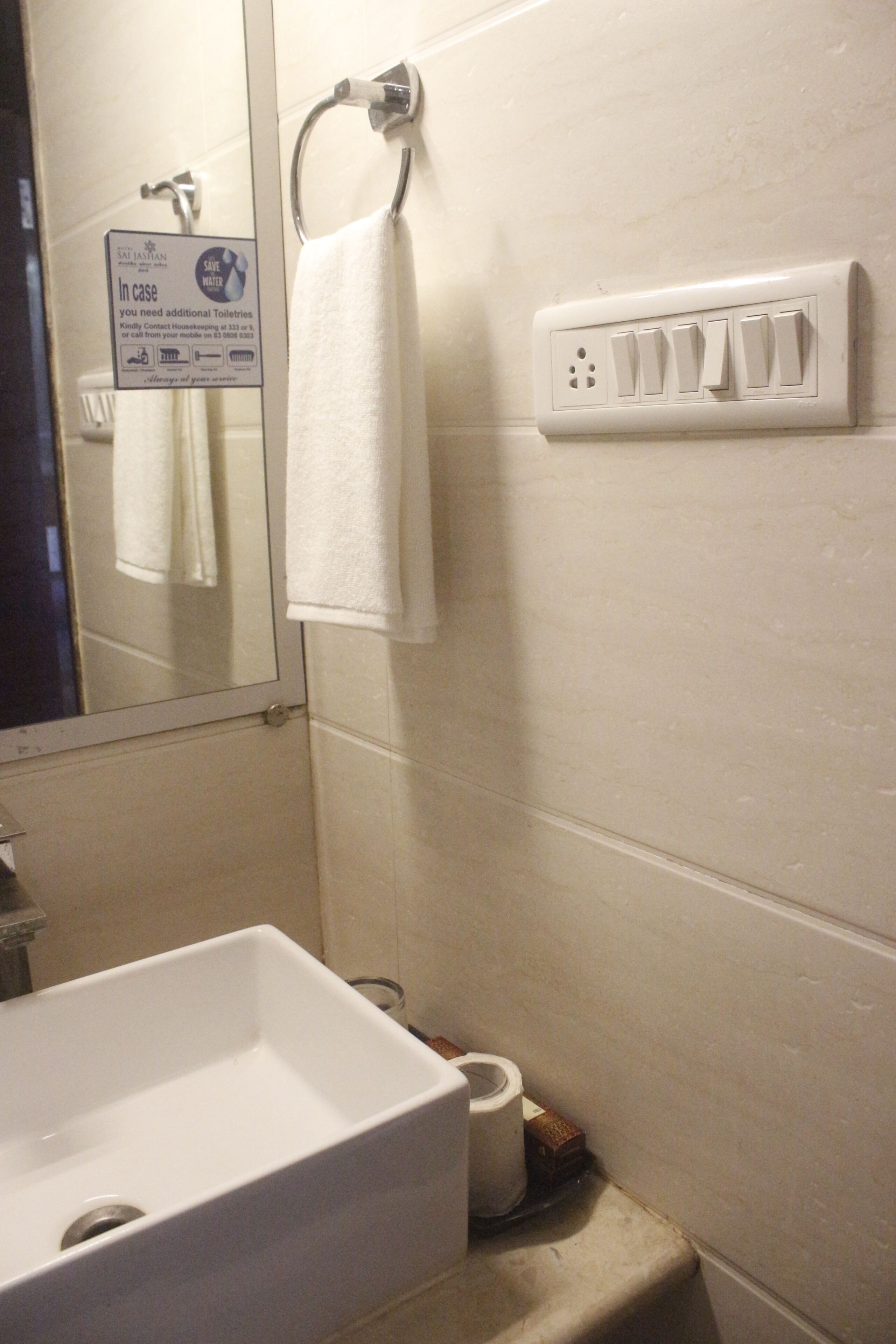 Een badkamer met een wastafel, een handdoekhouder, een spiegel en een stopcontact aan de muur.