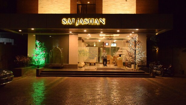 Exterior del hotel Sai Jashan con una entrada bien iluminada, una escalera que conduce a la puerta y un árbol de Navidad con luces.