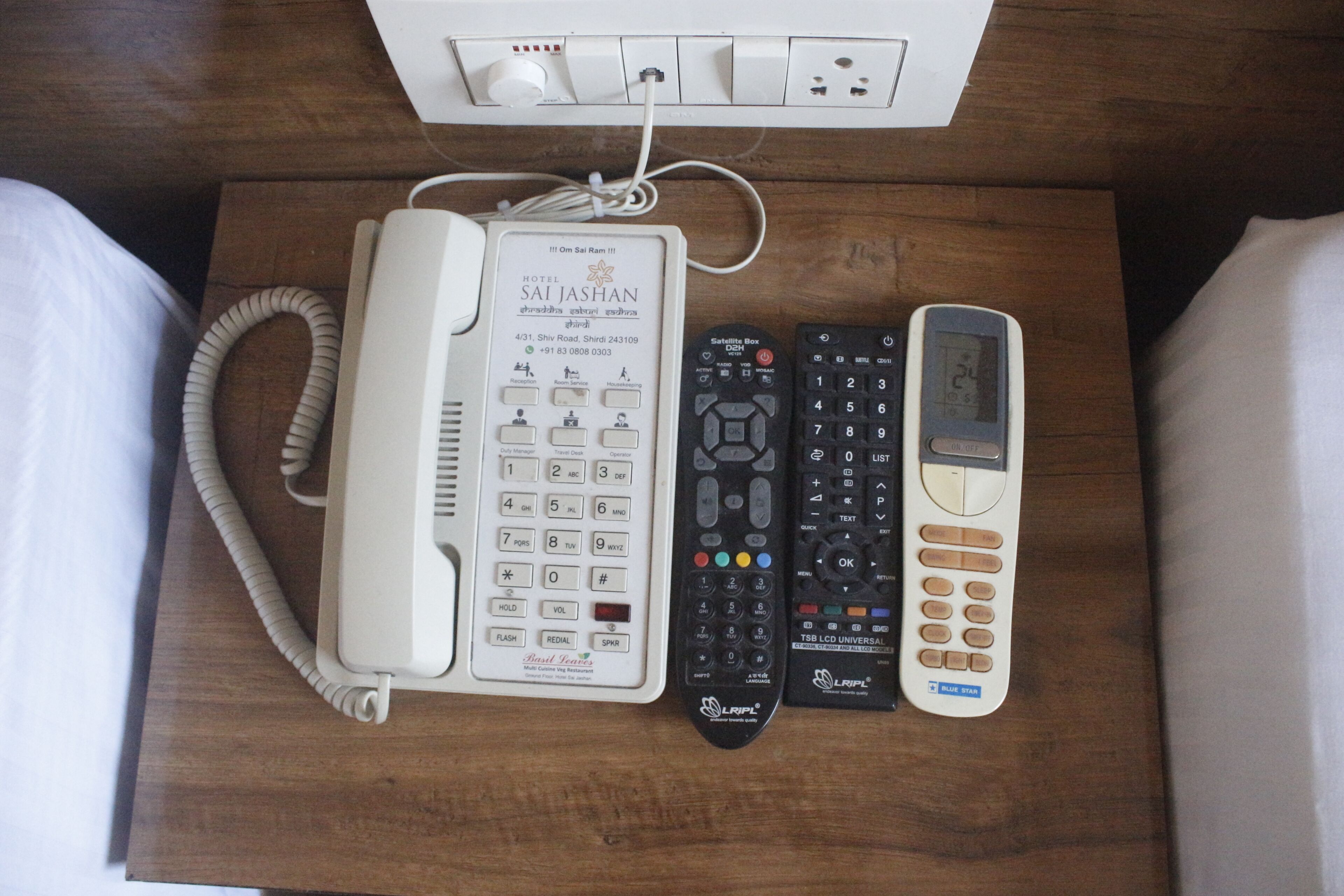 Habitación de hotel con un teléfono blanco, un teléfono satelital, un control remoto universal y un enchufe.
