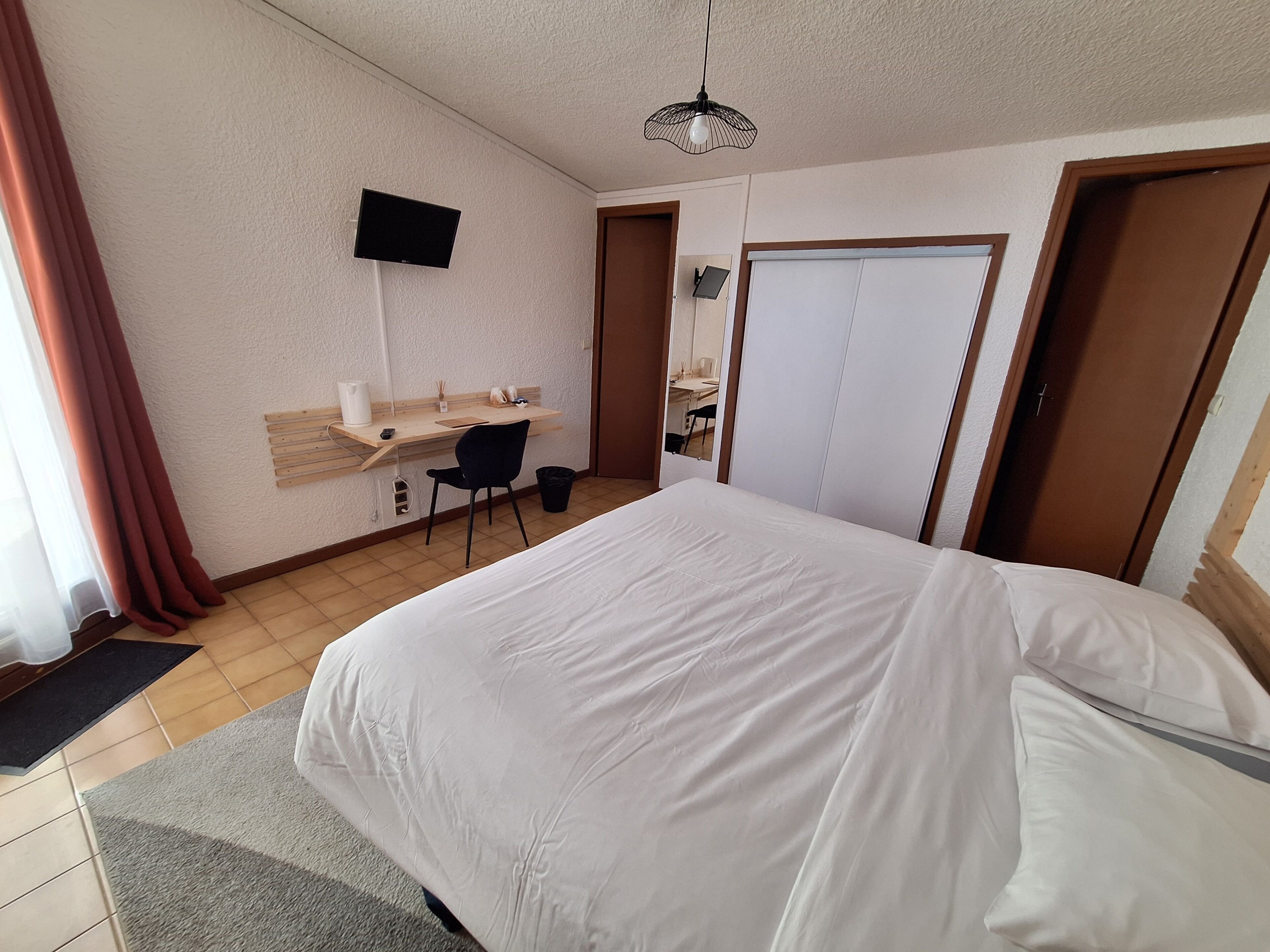 A hotel room with a bed, a desk, a chair, a TV, and a wardrobe.