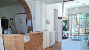 Zona de recepción con mostrador de madera, pared blanca con tablón de anuncios y vitrina de vidrio.