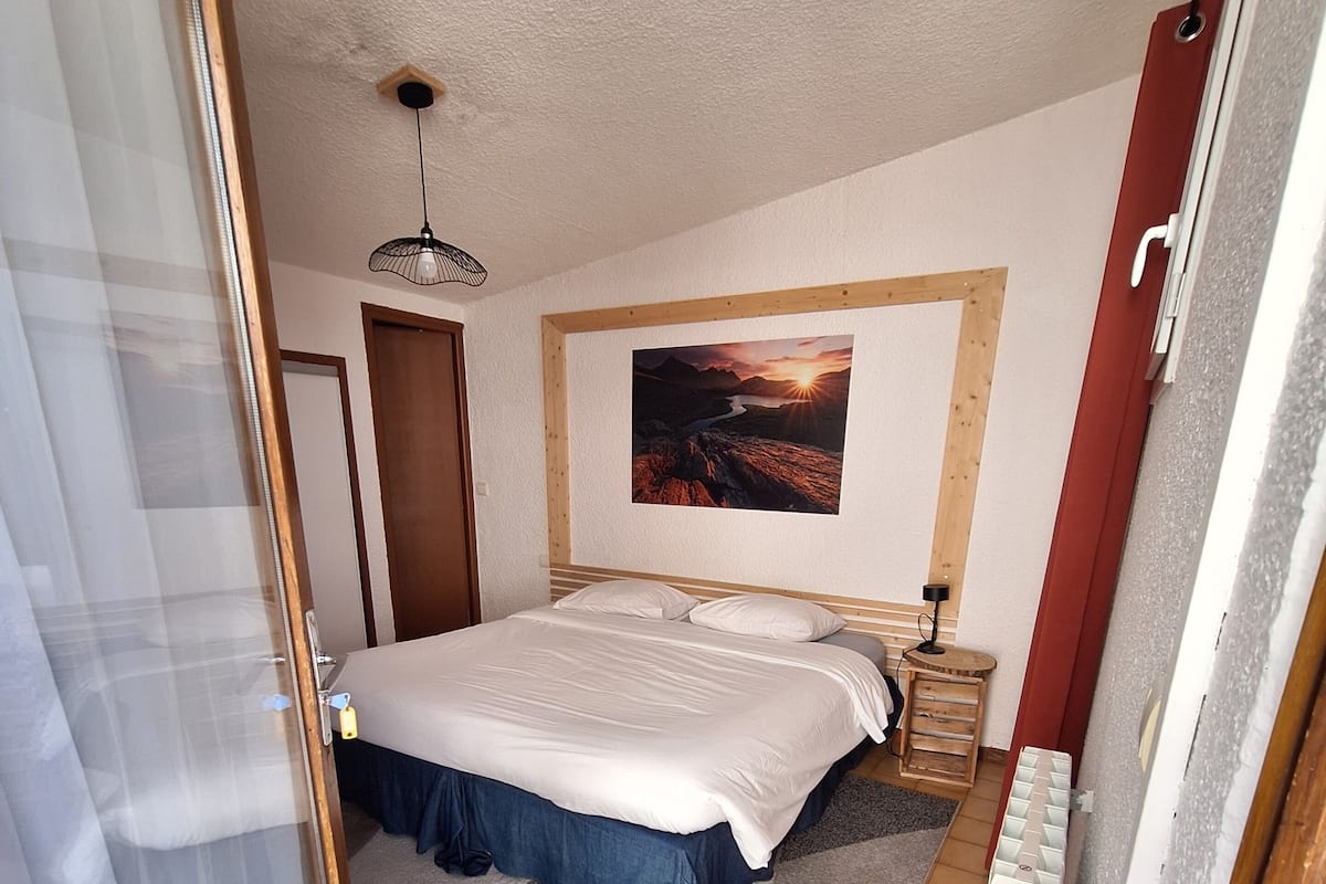 Ein Schlafzimmer mit einem Bett, einem Nachttisch, einer Lampe, einem Gemälde und einer Tür.