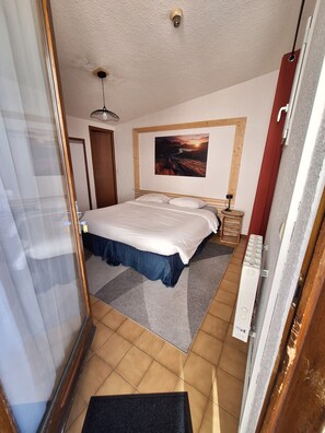 Un dormitorio con cama, mesita de noche, lámpara, cuadro y puerta.