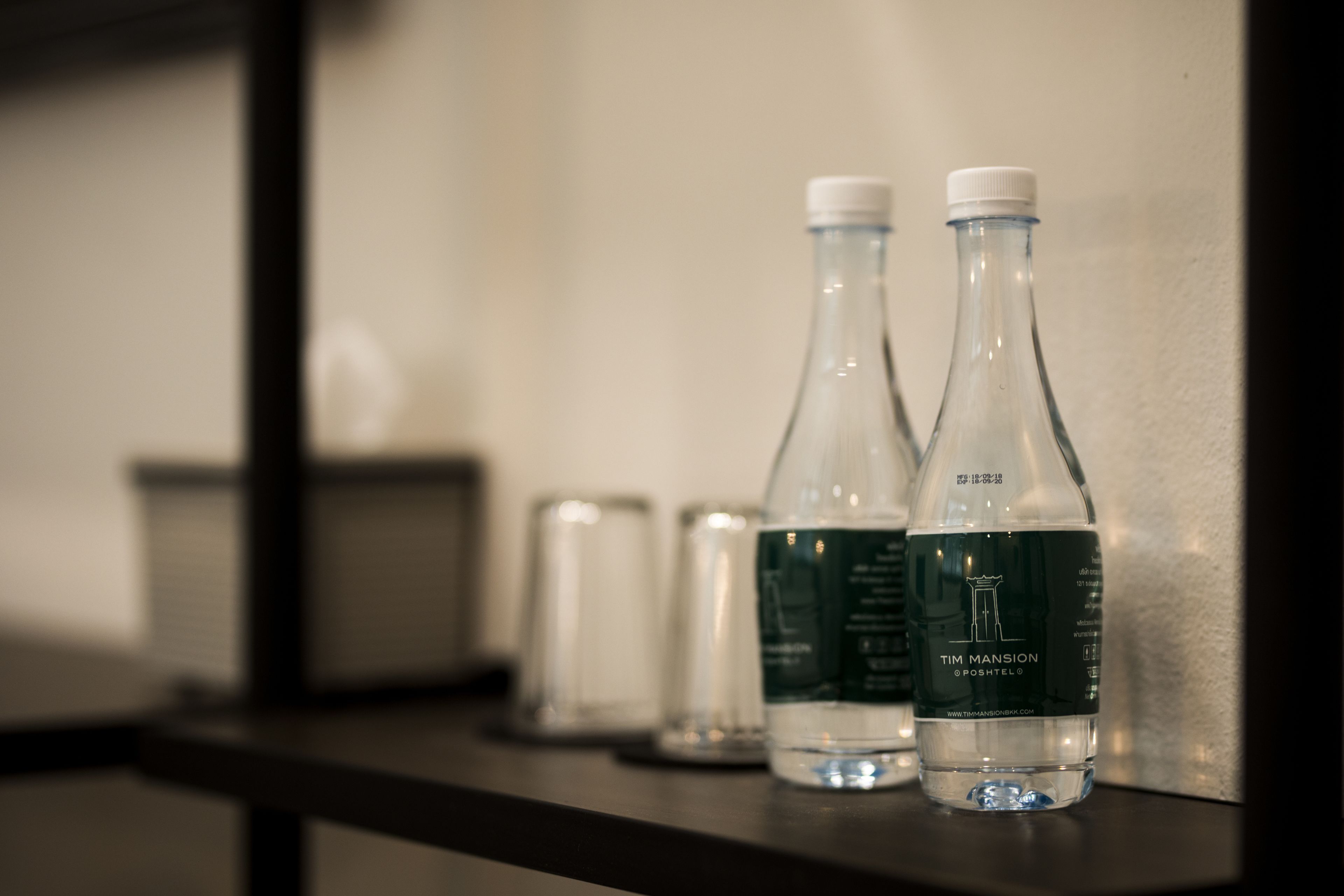 Two clear glass bottles with white caps on a dark surface, likely a bar area, with a blurred background.
