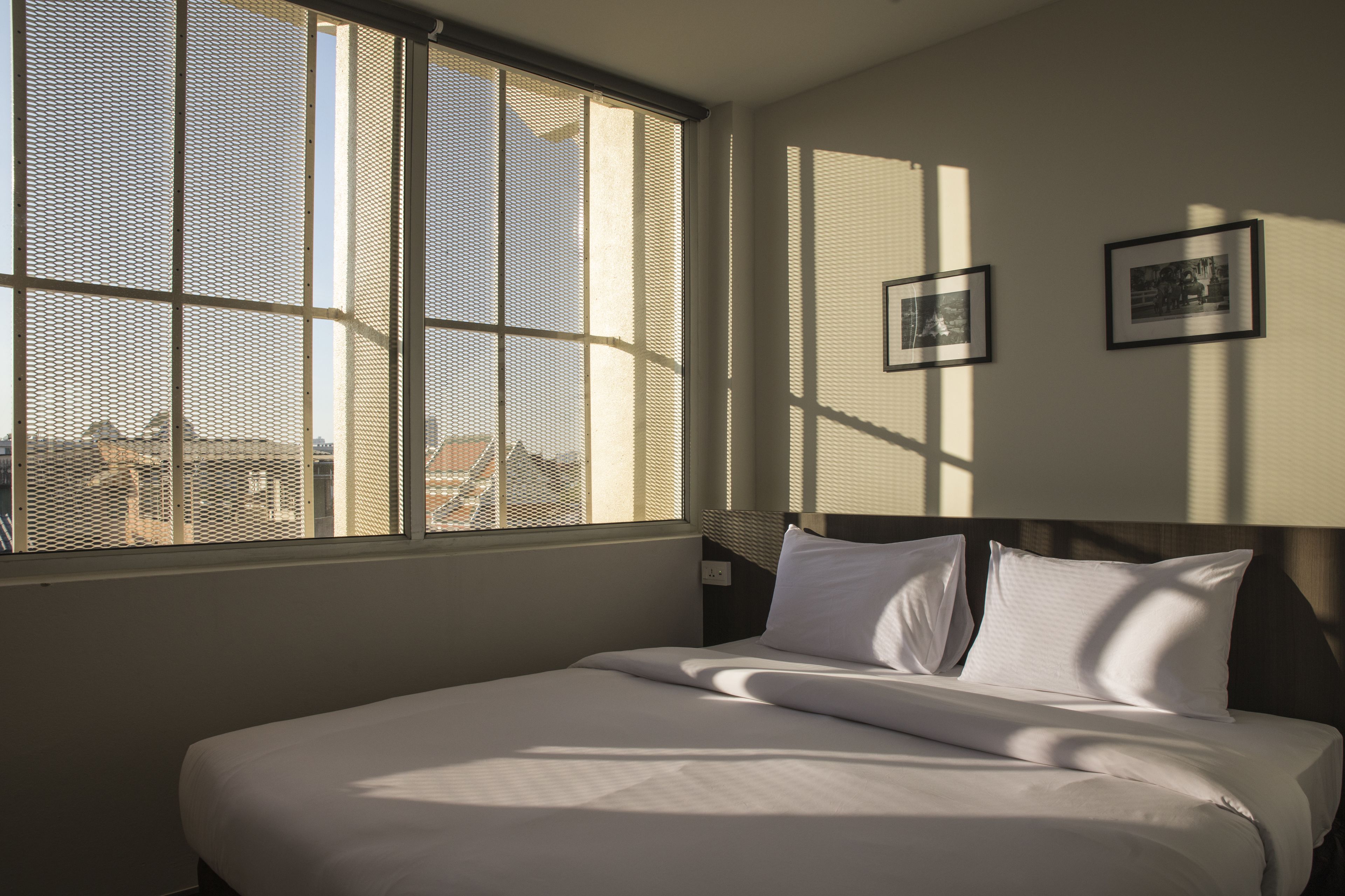 A hotel room with a large window, a bed with white linens, and two framed pictures on the wall.