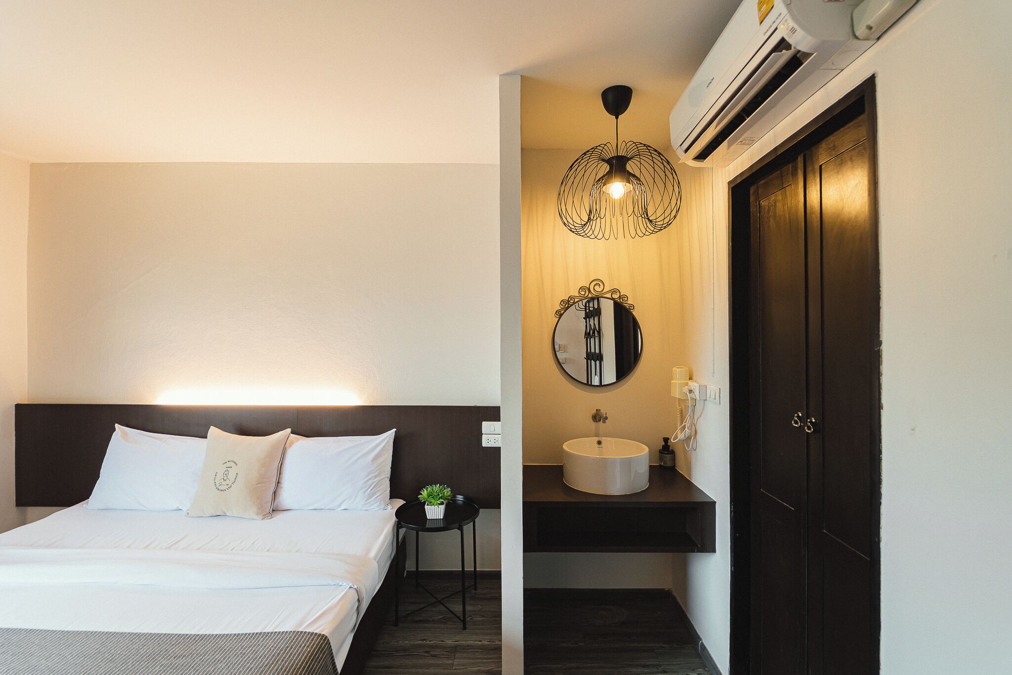 Ein Hotelzimmer mit Bett, Nachttisch und einem Badezimmer mit Waschbecken und Spiegel.