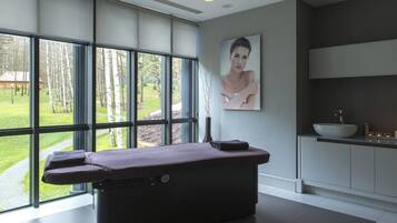 Un moderno spa con camilla de masaje, ventanas amplias, un lavabo y un cuadro.