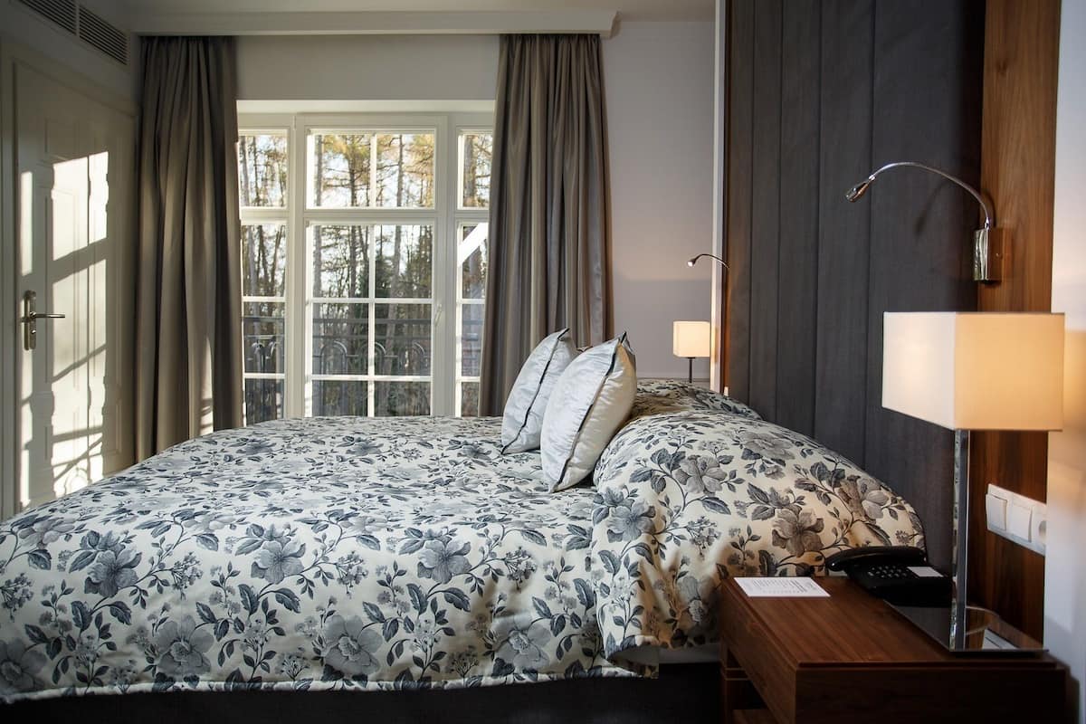 Une chambre à coucher avec un grand lit, deux lampes de chevet, une table de nuit en bois et une fenêtre avec des rideaux.