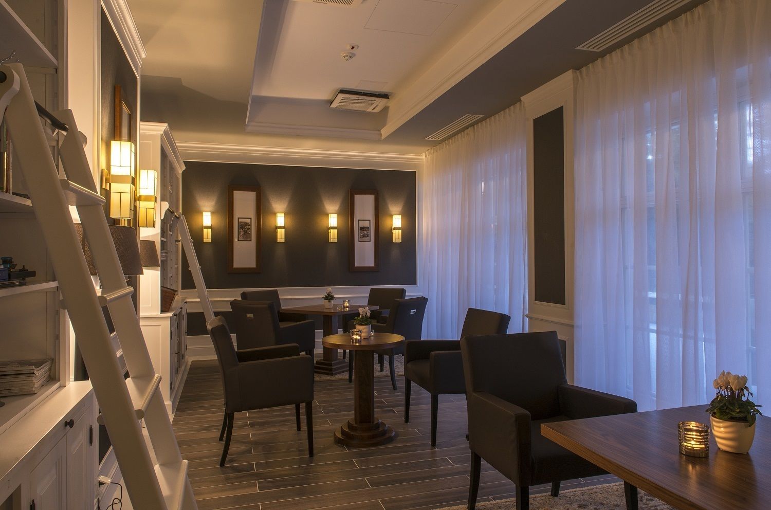 A modern hotel room with a dark wood floor, a dining area with a round table and chairs, and a staircase.